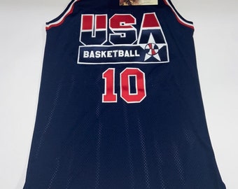 May include: A navy blue basketball jersey with the word "USA" in red, white, and blue letters. The jersey has the words "Basketball" and a star with a basketball inside. The number "10" is on the front of the jersey in red.