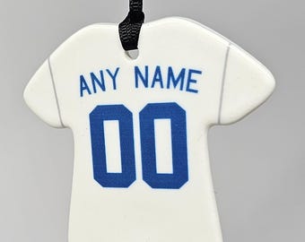 May include: White ceramic jersey-shaped ornament with the text "ANY NAME" above the number "00" in blue. A black cord is attached for hanging. The jersey has gray lines to simulate the seams.