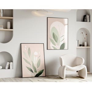 Könnte beinhalten: Zwei gerahmte abstrakte Kunstdrucke mit rosa Hintergrund und grünen Blättern. Die Drucke hängen an einer weißen Wand in einem modernen Wohnzimmer.