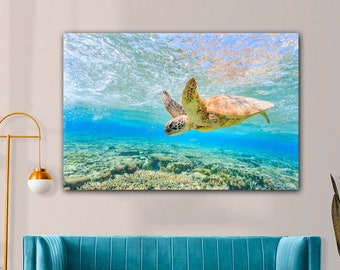 May include: A canvas print featuring an underwater scene with a sea turtle swimming in clear, turquoise water. The turtle has a brown shell and is surrounded by coral and sunlight. The artwork is displayed above a teal velvet sofa.