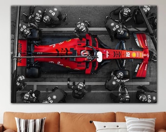 May include: A red Formula 1 race car with the number 19 on the side is being worked on by a team of mechanics wearing black uniforms. The car is surrounded by tools and equipment.