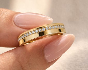 Könnte beinhalten: Ein goldener Ring mit einem Band aus kleinen, klaren Edelsteinen, die in einem Kanal gesetzt sind. Der Ring hat eine polierte, gelbgoldene Oberfläche. Die Edelsteine sind gleichmäßig angeordnet.