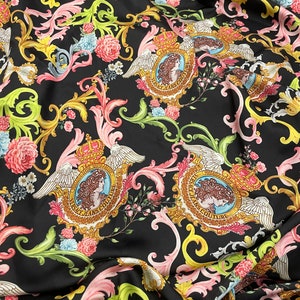 May include: Black fabric with a repeating pattern of gold, pink and green floral designs. The pattern also includes a repeated image of a crown, wings, and the text "Versace Jeans Couture".