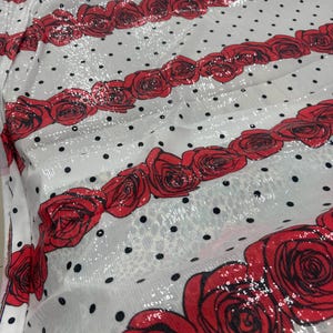 Puede incluir: Tela blanca con filas de rosas rojas y lunares negros. La tela tiene una textura de lentejuelas, lo que crea un efecto brillante. Las rosas están detalladas con contornos rojo oscuro y la tela está doblada.