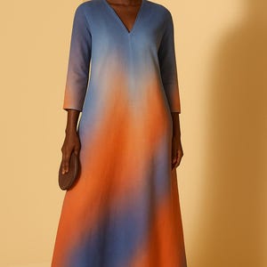 May include: A long, flowing dress with a V-neck and three-quarter sleeves. The dress features a gradient design, transitioning from blue at the top to orange in the middle and back to blue at the bottom. The model is wearing black sandals.