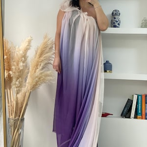 May include: A long, flowing ombre dress with a one-shoulder design. The dress is made of a sheer fabric and features a gradient of colors from light pink to purple.