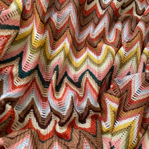 May include: A close-up of a colorful knitted fabric with a chevron pattern in shades of brown, red, pink, blue, green, and yellow.