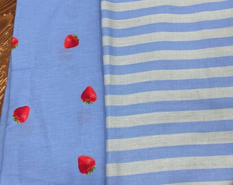 May include: Two fabric pieces: one light blue with embroidered red strawberries, the other with blue and white stripes. The strawberry fabric has several red strawberries scattered across its surface. The striped fabric has horizontal stripes.