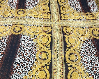 Puede incluir: Una tela con un patrón repetido de diseños barrocos dorados y estampado de leopardo. La tela es negra, blanca, dorada y marrón.