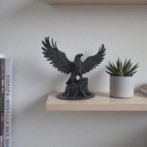 May include: A matte black eagle figurine with wings fully spread, perched atop a textured tree stump base. The sculpture is crafted with detailed feather patterns and a sharp beak, standing as a singular decorative object on a flat surface.