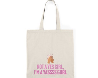May include: A beige tote bag with a pink graphic that says "Not a yes girl, I'm a yassss gurl" and a pink high five emoji.