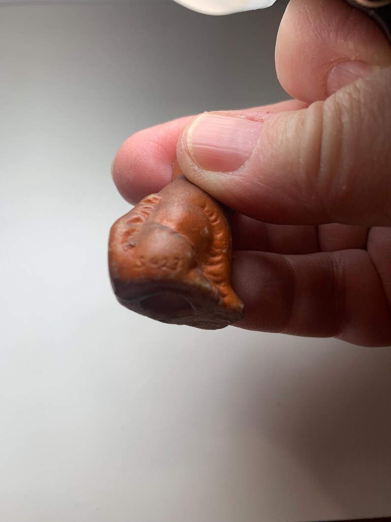 May include: A small, antique, brown ceramic figurine. The figurine has a detailed, textured surface with a rounded shape and a hole at the bottom. The number "3423" is visible on the front of the figurine.