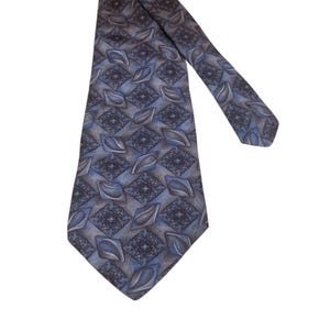 May include: A patterned necktie in shades of blue and gray. The tie features a repeating design of diamond shapes and leaf-like motifs. The tie is made of a smooth, possibly silk, material and is suitable for formal or business attire.