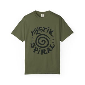 K&ouml;nnte beinhalten: Ein olivgr&uuml;nes Kurzarm-T-Shirt mit einem schwarzen Grafikdruck auf der Brust. Das Design besteht aus einer zentralen Spirale, die von dem Text "MYSTIK SPIRAL" in einer stilisierten, dekorativen Schriftart umgeben ist. Das T-Shirt hat einen Rundhalsausschnitt.