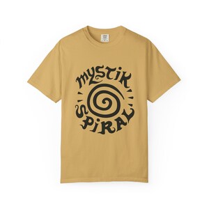 K&ouml;nnte beinhalten: Ein senfgelbes Kurzarm-T-Shirt mit einem schwarzen Grafikdruck auf der Brust. Das Design besteht aus einer zentralen Spirale, die von dem Text "MYSTIK SPIRAL" umgeben ist, welcher in einer stilisierten, dekorativen schwarzen Schriftart gehalten ist.