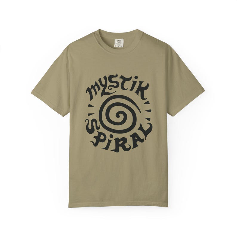 K&ouml;nnte beinhalten: Ein khakifarbenes Kurzarm-T-Shirt mit einem schwarzen Grafikdruck auf der Brust. Das Design besteht aus einer zentralen Spirale, die von dem Text "MYSTIK SPIRAL" in einer stilisierten, fetten und dunklen Schriftart umgeben ist.