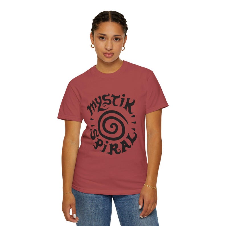 K&ouml;nnte beinhalten: Ein kurz&auml;rmeliges T-Shirt mit Rundhalsausschnitt in einem gedeckten Ziegelrot. Auf der Vorderseite befindet sich ein gro&szlig;es, kr&auml;ftiges schwarzes Grafikdesign, das aus einer zentralen Spirale und dem Schriftzug "MYSTIK SPIRAL" in stilisierter Schrift besteht.