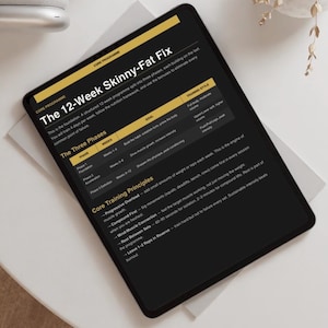 Può includere: Un tablet nero mostra un programma di fitness intitolato "The 12-Week Skinny-Fat Fix". Lo schermo mostra fasi, obiettivi e principi di allenamento. Il tablet è su una superficie chiara.
