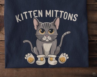 May include: A navy blue t-shirt with a cartoon gray cat wearing white booties. The text "Kitten Mittons" is printed on the shirt.
