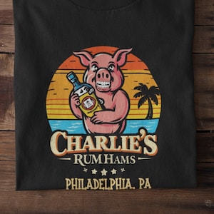 May include: Black t-shirt with a cartoon pig holding a bottle of rum in front of a sunset. The text "Charlie's Rum Hams Philadelphia, PA" is printed below the pig.