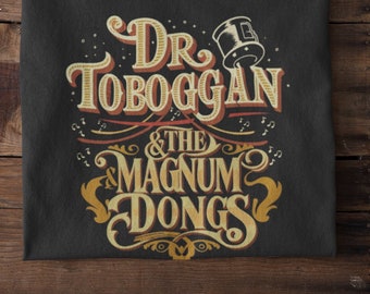 May include: Black t-shirt with a vintage-style graphic design featuring the text "Dr. Toboggan & The Magnum Dongs" in gold and yellow lettering.