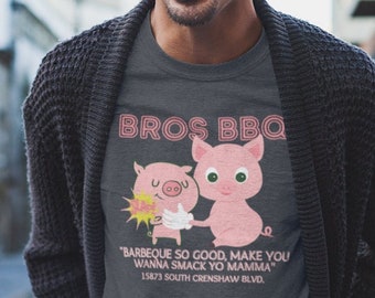 May include: A dark gray t-shirt with the text "BROS BBQ" and a cartoon pig graphic. Below the graphic is the text "BARBEQUE SO GOOD, MAKE YOU WANNA SMACK YO MAMMA" and the address "15873 SOUTH CRENSHAW BLVD."