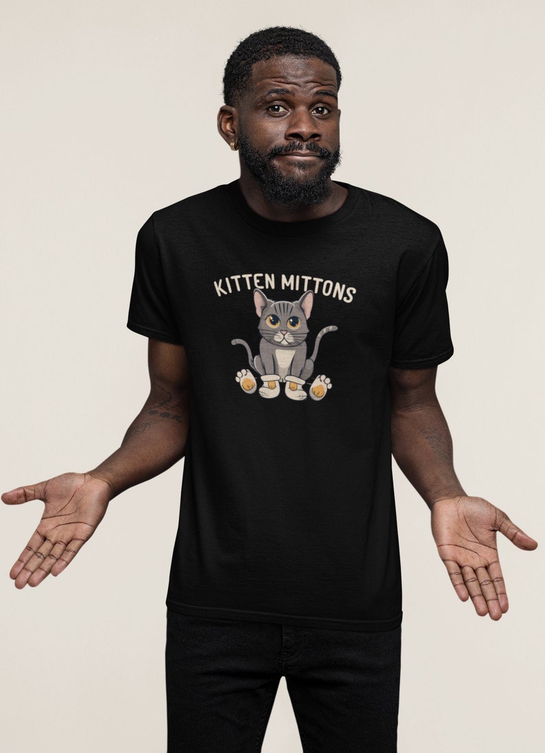 May include: A black t-shirt featuring the text "Kitten Mittons" and a cartoon image of a grey cat wearing mittens.