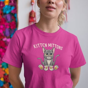 May include: A pink t-shirt featuring a cartoon cat wearing mittens and the text "Kitten Mittons".