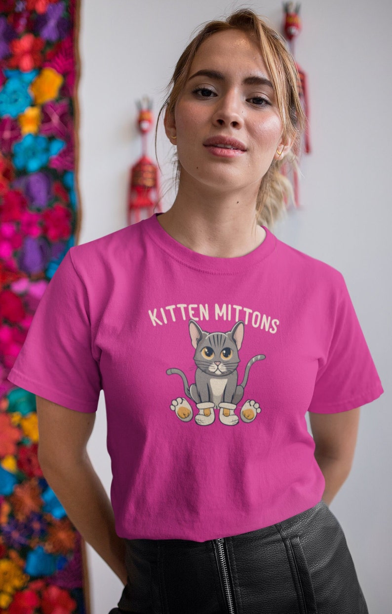 May include: A pink t-shirt featuring a cartoon cat wearing mittens and the text "Kitten Mittons".