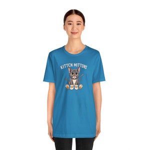 May include: A turquoise blue t-shirt with a white graphic of a grey cat wearing orange mittens and the text "Kitten Mittons".