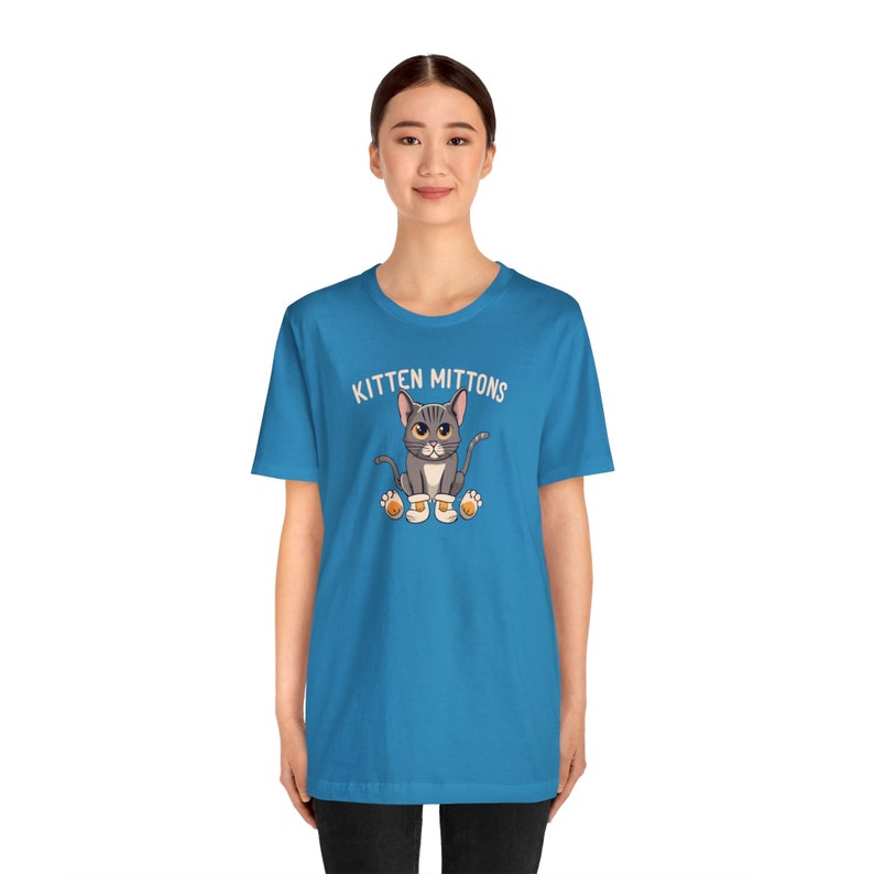 May include: A turquoise blue t-shirt with a white graphic of a grey cat wearing orange mittens and the text "Kitten Mittons".