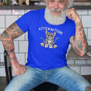May include: A man wearing a royal blue t-shirt with a cartoon cat wearing mittens and the text "Kitten Mittons".