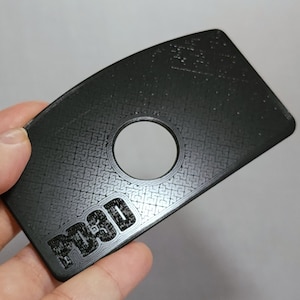 Puede incluir: Un objeto de plástico negro con una superficie texturizada y un agujero circular en el centro. El objeto tiene la palabra "F13D" impresa en él.