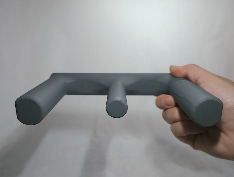 May include: A gray plastic wall-mounted holder with three rounded hooks. The holder is designed to hold items like towels, robes, or other items.