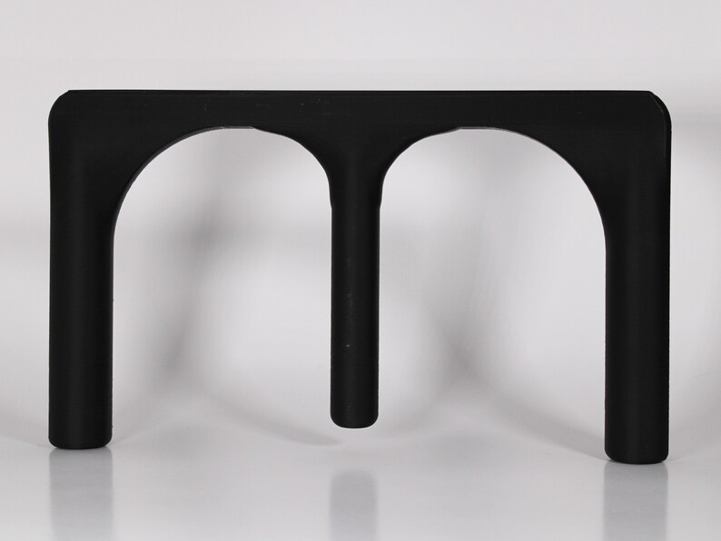 May include: Black plastic stand with two arches, designed to hold two items.