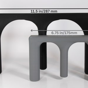 May include: Two black and grey plastic stands with arched openings. The larger stand measures 11.5 inches wide and the smaller stand measures 6.75 inches wide.