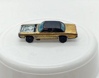 May include: A gold diecast toy car with a black roof and a partially open hood. The car has a detailed engine and black wheels.