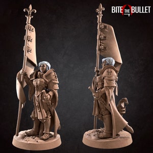 May include: A miniature figurine of a female warrior in armor holding a flag with a fleur-de-lis design. The flag is attached to a staff with a fleur-de-lis finial. The warrior is wearing a helmet and a long, flowing cloak. The figurine is painted in a brown and white color scheme. The figurine is standing on a circular base. The text "BITE THE BULLET" is visible in the background.