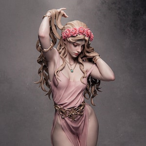 May include: A statue of a woman with long, flowing blonde hair, wearing a pink dress and a floral crown. The statue has gold bracelets and a decorative belt. A necklace with a turquoise pendant is also visible. The woman is looking down with a serene expression.