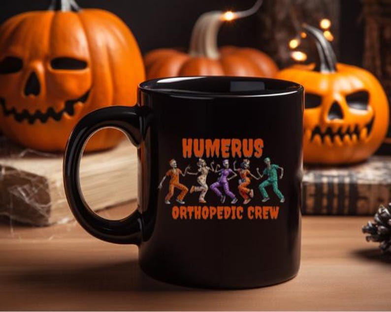 K&ouml;nnte beinhalten: Schwarze Keramik-Tasse mit dem Text "HUMERUS ORTHOPEDIC CREW" und einer Grafik von tanzenden Skeletten in Orange, Lila und Gr&uuml;n. Der Hintergrund zeigt geschnitzte orangefarbene K&uuml;rbisse, was auf ein Halloween-Thema hindeutet.