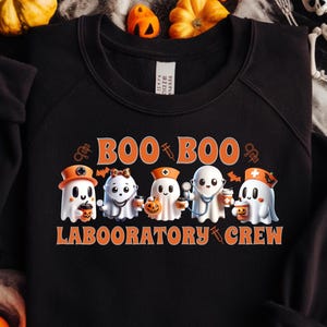 May include: Black crewneck sweatshirt with a Halloween-themed graphic. The design features cartoon ghosts dressed as medical professionals with the words "BOO BOO LABORATORY CREW" in orange and white.