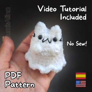 May include: A white, plush, cat-shaped amigurumi with black embroidered facial features. The image includes the text "Video Tutorial Included", "No Sew!", and "PDF Pattern". The amigurumi is held in a hand.