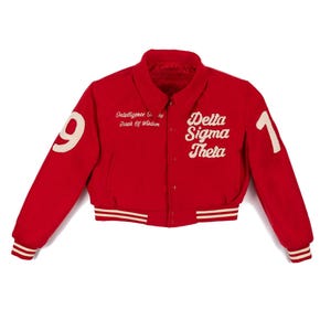 Op de afbeelding: Rode varsity jas met witte letters en accenten. De jas heeft de tekst "Delta Sigma Theta" en "Intelligence is the Torch of Wisdom". De mouwen tonen de cijfers "9" en "1".