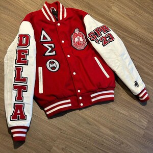 May include: Red and white varsity jacket with the word "DELTA" on the left sleeve and "SPR 23" on the right sleeve. The jacket features a crest and Greek letters on the chest.