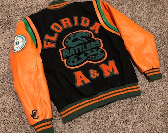 May include: Black and orange varsity jacket with green detailing. The back displays "FLORIDA RATTLES" and "A&M" lettering with a snake logo. The sleeves are orange leather. A patch is on the left sleeve.