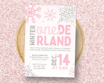 May include: A pink and white invitation with the text "Winter One-derland" and snowflake graphics. The invitation includes event details: date, time, and RSVP information. The invitation is on a wooden tray, set against a pink glitter background.