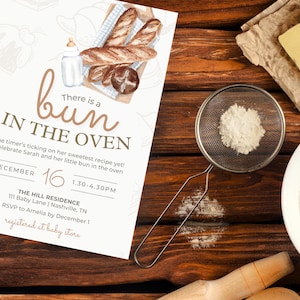 May include: A baby shower invitation with the text "There is a bun in the oven." The invitation features watercolor illustrations of bread, a baby bottle, and a decorative font. The date and time of the event are also included.