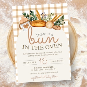 May include: A baby shower invitation with a watercolor design. The invitation features the text "There is a bun in the oven" with decorative bread and greenery. The date and time are included, along with RSVP information.