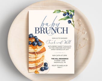 May include: A baby brunch invitation card featuring a stack of pancakes topped with blueberries and syrup. The words "baby brunch" are written in elegant script. The invitation includes details for the event, such as the date, time, and location.