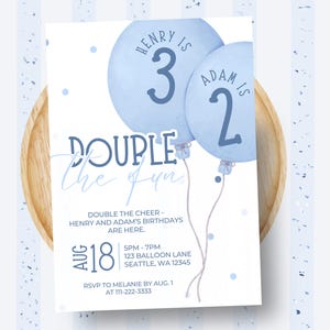 Puede incluir: Una invitación de cumpleaños azul claro con dos globos de acuarela. La invitación dice "Double the Fun" e incluye los nombres Henry y Adam, con sus edades y los detalles del evento. La invitación está sobre un plato de madera.